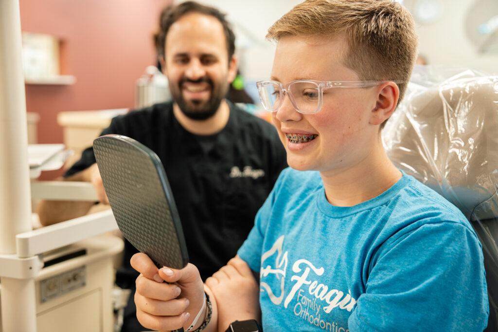Dr. Kyle Feagin smiling as a young patient checks his new braces in a hand mirror